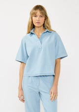 [Color: Light Denim Blue] A front facing image of  blonde model wearing a cotton short sleeve shirt with a half button front and a collared neck. Styled with matching bottoms. 