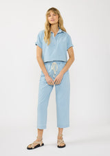 [Color: Light Denim Blue] A front facing image of  blonde model wearing a cotton short sleeve shirt with a half button front and a collared neck. Styled with matching bottoms. 