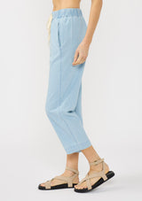 [Color: Light Denim Blue] A side facing image of a blonde model wearing a casual light blue cropped pant with an elastic waistband, drawstring, and side pockets. 
