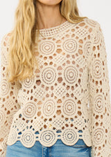 [Color: Natural] A detail image of a blonde model wearing a circular crochet knit top with a round neckline and long sleeves. A spring boho top for casual and beach styling. 