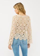 [Color: Natural] A back facing image of a blonde model wearing a circular crochet knit top with a round neckline and long sleeves. A spring boho top for casual and beach styling. 