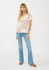 [Color: Blush/Dusty Blue] A front facing image of a blonde model wearing a pink floral top with layered short sleeves and a split v-neckline. A spring feminine top for casual outings. 