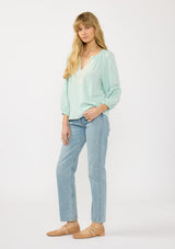 [Color: Dusty Mint] A side facing image of a blonde model wearing a mint green boho blouse with embroidered and lace details. 