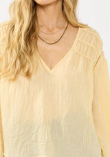 [Color: Sunshine] A detail image of a blonde model wearing a boho yellow blouse with a v neckline, shirred shoulder detail, and long sleeves. 