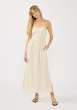 [Color: Natural] A front facing image of a blonde model wearing a beige linen blend maxi dress with a halter neck, side pockets, and a back zip up closure. 