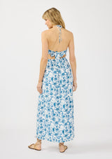 [Color: Ivory/Navy] A back facing image of a blonde model wearing a blue and white floral maxi dress with a smocked top, halter neckline, front slits, and tie back detail.
