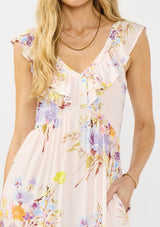 [Color: Blush/Dusty Blue] A detail image of a blonde model wearing a pink floral print maxi dress with ruffled sleeves, adjustable straps, and side pockets. 