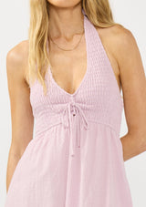 [Color: Lilac] A detail image of a blonde model wearing a light purple pink maxi dress with a smocked halter neckline, v neckline, and side pockets. 