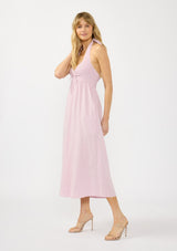 [Color: Lilac] A side facing image of a blonde model wearing a light purple pink maxi dress with a smocked halter neckline, v neckline, and side pockets. 