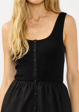 [Color: Black] A detail image of a blonde model wearing black tank dress with a soft knit top and contrast cotton skirt. Featuring side pockets and a button front. 