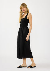 [Color: Black] A side facing image of a blonde model wearing black tank dress with a soft knit top and contrast cotton skirt. Featuring side pockets and a button front. 
