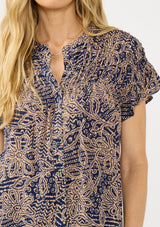 [Color: Navy/Natural] A detail image of a blonde model wearing a navy and natural floral print top with short ruffled sleeves, a button front, and a shirred yoke. 