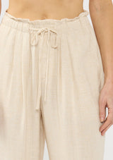 [Color: Natural] A detail image of a blonde model wearing a beige crochet vest, tank top, and wide-leg pants with a drawstring waist and side pockets.
