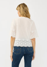 [Color: White] A back facing image of a blonde model wearing a short sleeve top with embroidered eyelet, an open front with ties, and a v neckline.  