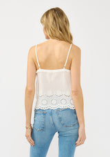 [Color: White] A back facing image of a blonde model wearing a white cami with an eyelet hem, v neckline with ruffle trim, and adjustable spaghetti straps. 