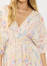 [Color: Almond/Rose] A front facing image of a blonde model wearing a pink and yellow boho print maxi dress with kimono sleeves, a smocked waist, a tie back detail, and side slits. The perfect vacation dress. 