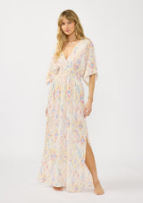 [Color: Almond/Rose] A front facing image of a blonde model wearing a pink and yellow boho print maxi dress with kimono sleeves, a smocked waist, and side slits. The perfect vacation dress. 