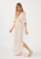 [Color: Almond/Rose] A side facing image of a blonde model wearing a pink and yellow boho print maxi dress with kimono sleeves, a smocked waist, a tie back detail, and side slits. The perfect vacation dress. 
