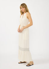 [Color: Natural] A side facing image of a blonde model wearing a beige bohemian sleeveless maxi dress with a button front top, waist belt, side pockets, and contrast stitching. 
