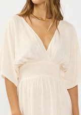 [Color: Natural/Coral] A detail image of brunette model wearing a kimono sleeve maxi dress with a coral floral border print, smocked waist, a v-neckline, and side slits.