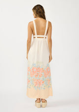[Color: Natural/Coral] A back facing image of a brunette model wearing a coral floral border print maxi dress with a sleeveless design, side pockets. v neckline, and elastic straps. 