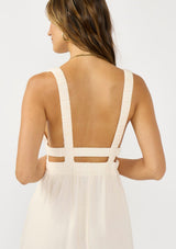 [Color: Natural/Coral] A detail image of a brunette model wearing a coral floral border print maxi dress with a sleeveless design, side pockets. v neckline, and elastic straps. 