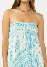 [Color: Natural/Mint] A detail image of a brunette model wearing a sleeveless mint green floral maxi dress with a tiered silhouette, high low hemline, ruffle trims, and side pockets. 