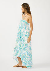 [Color: Natural/Mint] A side facing image of a brunette model wearing a mint green floral maxi dress with a halter neckline, tiered silhouette, high low hemline, ruffle trims, and side pockets. 