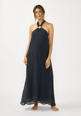 [Color: Slate Blue] A front facing image of a brunette model wearing a relaxed crinkled texture maxi dress with an o ring and halter neckline. 