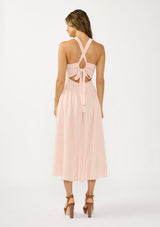 [Color: Shell Pink] A back facing image of a brunette model wearing a sleeveless smocked midi dress with a round neck, side pockets, and a cross back with tie detail. 