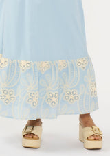 [Color: Chambray Blue/Natural] A detail image of a light blue maxi skirt with a smocked waist and embroidered hem. 