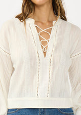 [Color: Natural] A detail image of a brunette model wearing a white textured cotton blouse with a lace up front, lace insert, and long sleeves with dropped shoulders. 
