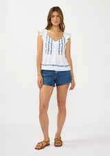 [Color: White/Blue] A front facing image of a brunette model wearing a white flutter sleeve top with blue floral embroidery, a button front, and pintucks. 