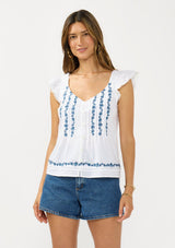 [Color: White/Blue] A front facing image of a brunette model wearing a white flutter sleeve top with blue floral embroidery, a button front, and pintucks. 