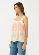 [Color: Natural/Coral] A side facing image of a brunette model wearing a coral floral tank top with solid back and a square neckline. 