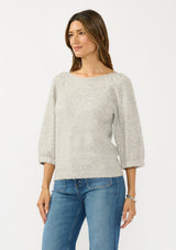 [Color: Light Heather Grey] A side facing image of a brunette model wearing a grey sweater with a crew neckline and three quarter length sleeves. 