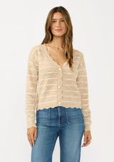 [Color: Heather Sand/White] A front facing image of a brunette model wearing a light brown pointelle sweater with a v-neckline, button front, and a scalloped trim. 