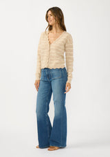 [Color: Heather Sand/White] A side facing image of a brunette model wearing a light brown pointelle sweater with a v-neckline, button front, and a scalloped trim. 