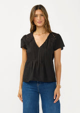 [Color: Black] A front facing image of a brunette model wearing a lightweight black top with embroidered cutouts, pintucks, and a v neckline. 