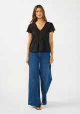 [Color: Black] A front facing image of a brunette model wearing a lightweight black top with embroidered cutouts, pintucks, and a v neckline. 