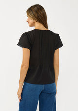 [Color: Black] A back facing image of a brunette model wearing a lightweight black top with embroidered cutouts, pintucks, and a v neckline. 