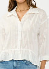 [Color: White] A front facing detail image of a brunette model wearing a white striped blouse with a button front, collared neck, and a high low hemline with ruffle trim.