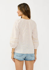 [Color: Tan/Natural] A back facing image of a brunette model wearing a beige checkered blouse with floral embroidery, lace details, and a split v neckline with ties. 