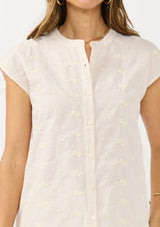 [Color: Tan/Natural] A detail image of a brunette model wearing a checkered button front top with cap sleeves and floral embroidery. 