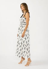 [Color: White/Black] A side facing image of a brunette model wearing a white and black floral eyelet midi dress with tie shoulders, a square neckline, and a gathered bodice.