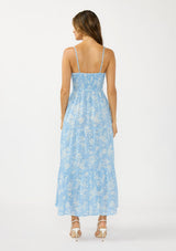 [Color: Blue/Ivory] A back facing image of a brunette model wearing a blue and white floral maxi dress with a scoop neckline, adjustable spaghetti straps, button front, and side pockets. 