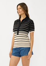 [Color: Black/Buttercream] A side facing image of a brunette model wearing a black and beige collared sweater top with a striped design, a button front, and short sleeves. 