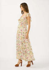 [Color: Blush/Rose] A side facing image of a brunette model wearing a pink and green floral maxi dress with a ruffled top, v neckline, elastic waist, and a tiered skirt with a slit. 