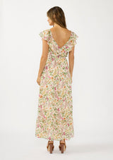 [Color: Blush/Rose] A back facing image of a brunette model wearing a pink and green floral maxi dress with a ruffled top, v neckline, elastic waist, and a tiered skirt with a slit. 