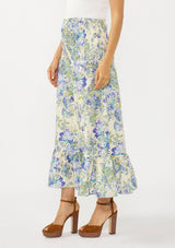 [Color: Cream/Dusty Lilac] A side facing image of a brunette model wearing a cream and purple floral skirt with a smocked waist. Styled with a white bodysuit. 